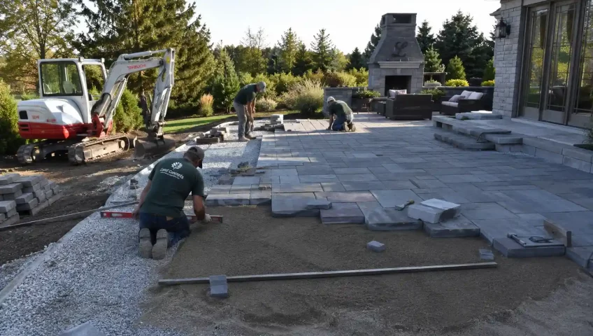 Modern backyard patio construction project with stone pavers, retaining walls, outdoor seating, and landscaping in progress.